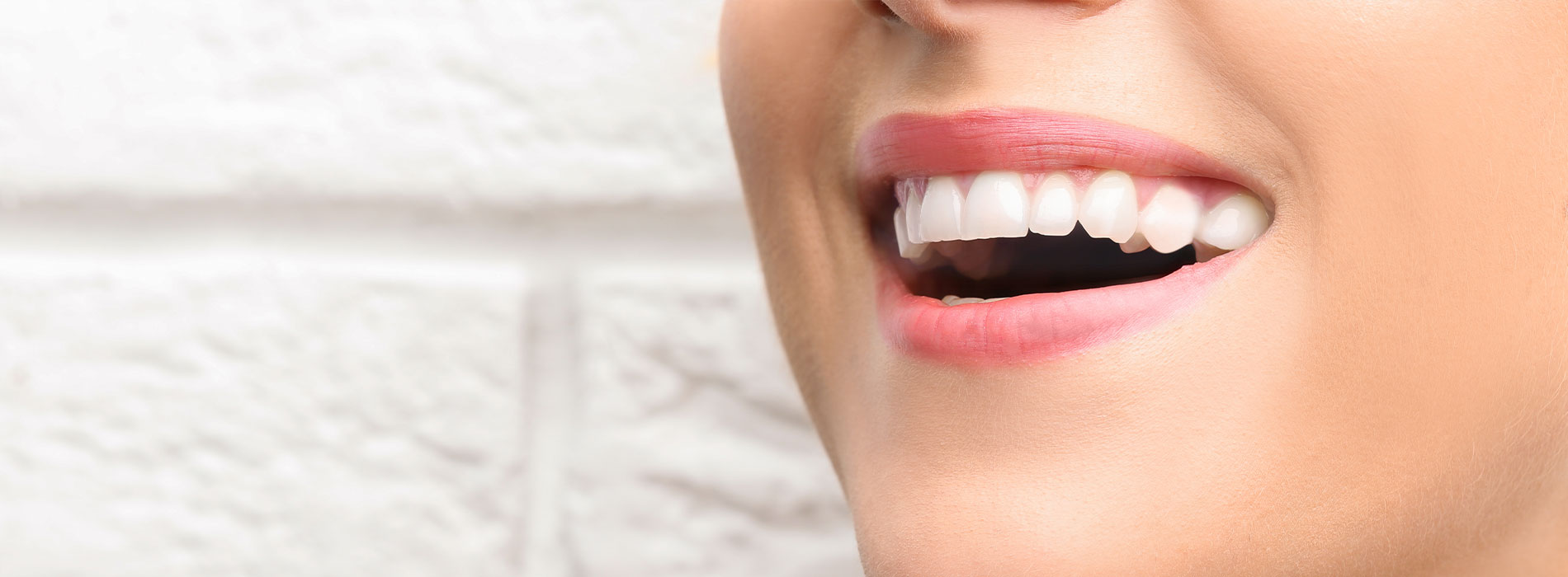 The image shows a close-up of a person s smiling face with their teeth visible, taken from the chin up against a blurred background.