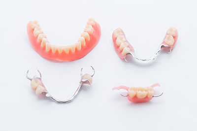 The image shows a set of dentures with visible teeth and gums placed on a white background, accompanied by a pair of scissors.